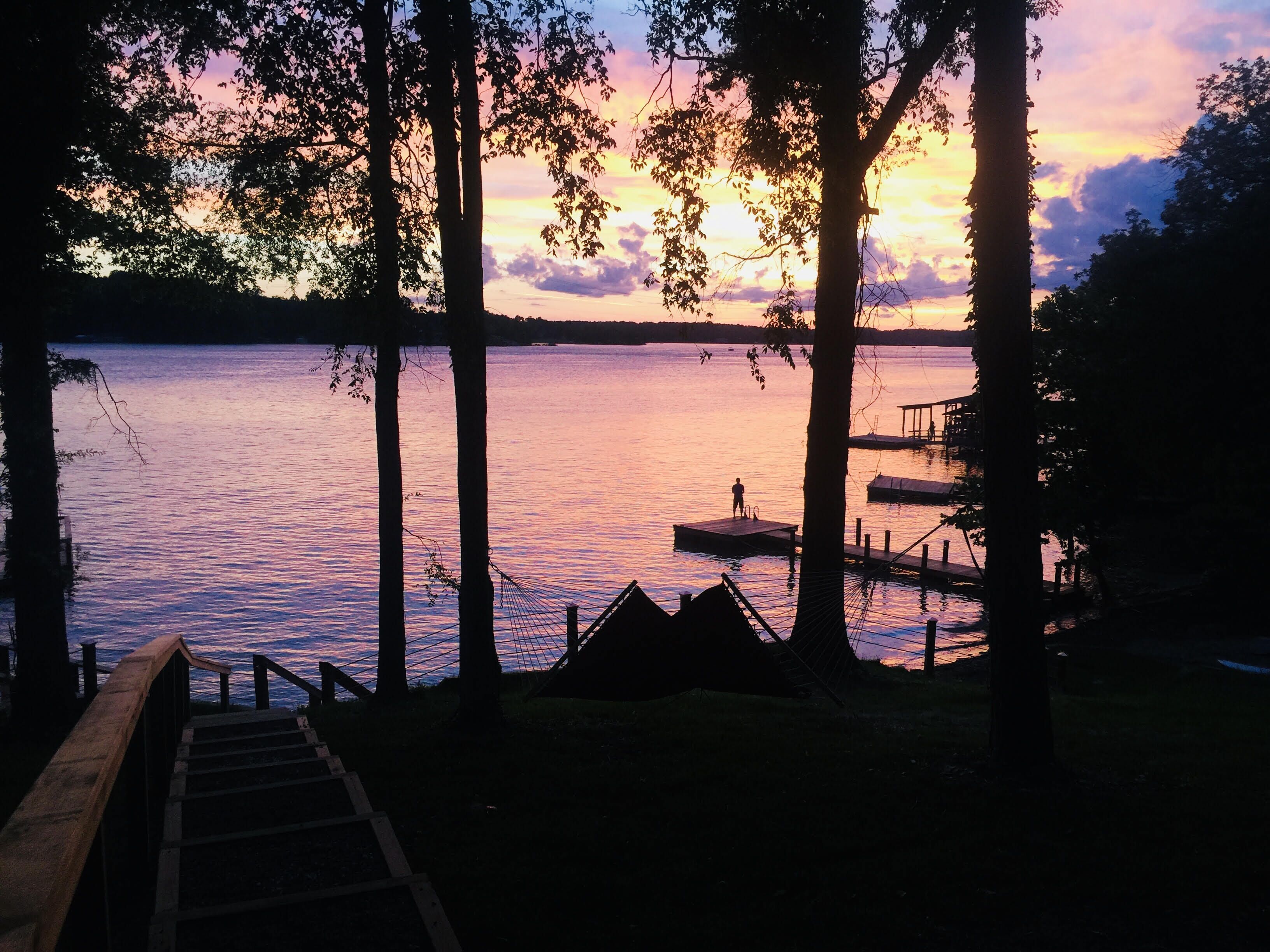 A wooden dock extending into a calm lake at sunset, surrounded by trees.