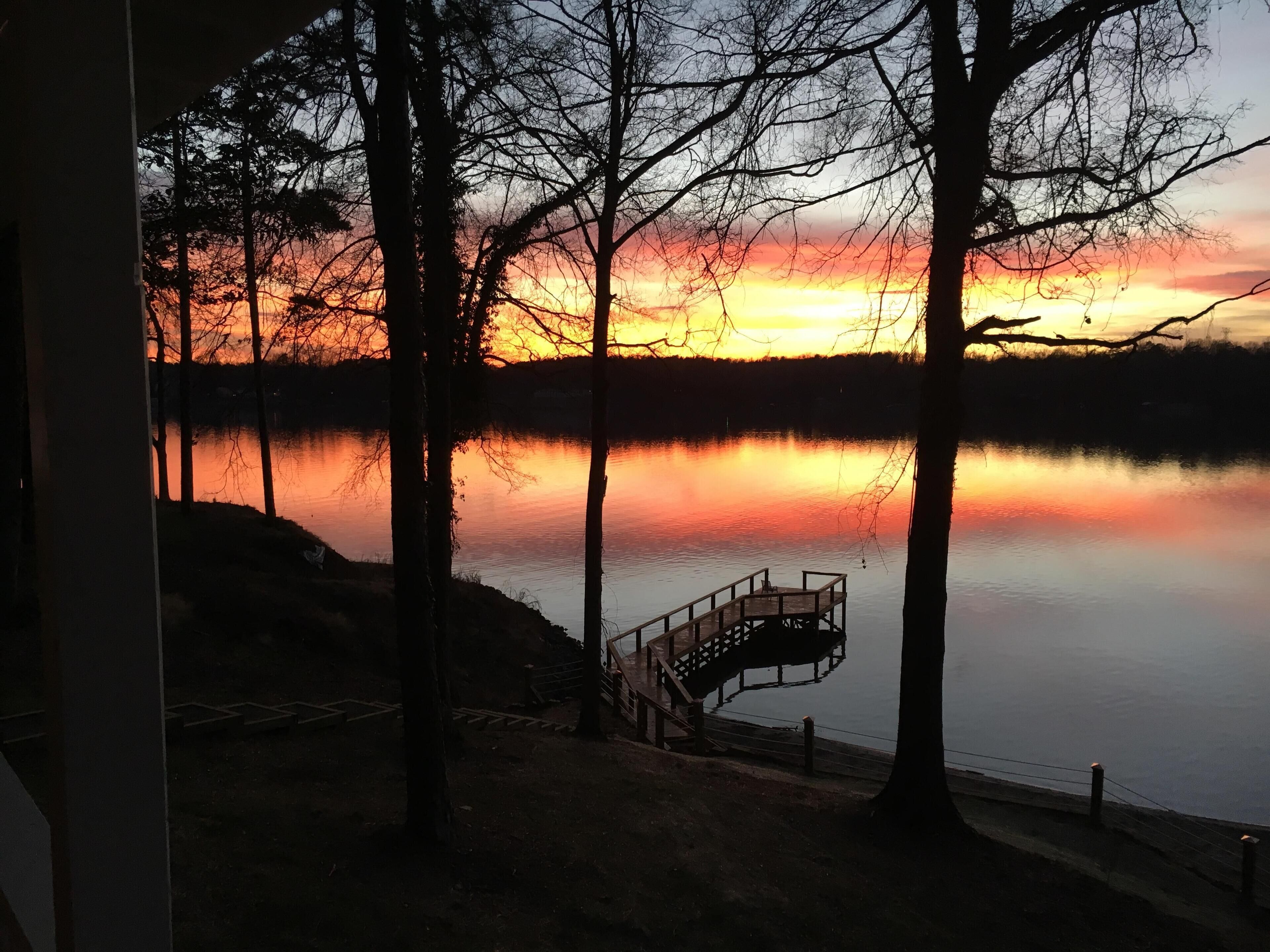 Ein Sonnenuntergangblick vom Fenster auf einen See, mit einem hölzernen Steg und Bäumen.