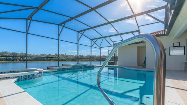 An indoor swimming pool with clear blue water, surrounded by a glass enclosure, and a view of a lake and trees in the background. - Near Disney and USTA tennis campus - Pool Villa on the Lake - Stunning Views! (Kissimmee)