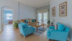 A spacious living room with a blue sofa set, a brown sofa, and a coffee table. There are two framed pictures on the wall and a potted plant on the floor. - Near Disney and USTA tennis campus - Pool Villa on the Lake - Stunning Views! (Kissimmee)