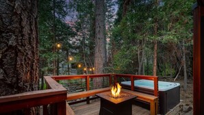 Una terraza con una chimenea, asientos y un jacuzzi en un área boscosa.