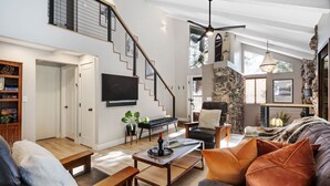 Un amplio espacio de sala con una escalera, una chimenea y un televisor montado en la pared.