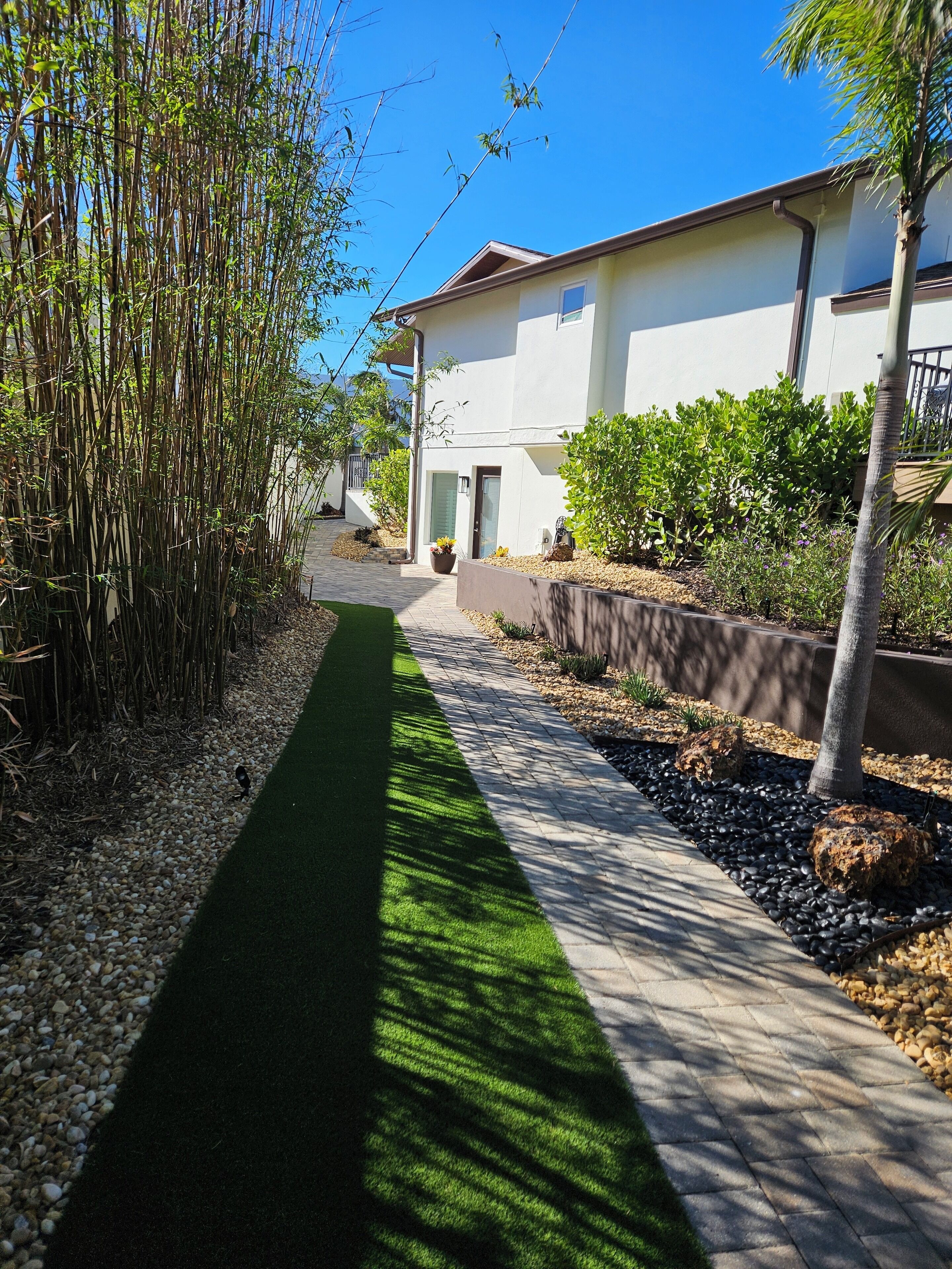 Un vialetto conduce a una casa moderna con facciata bianca, immersa nel verde e circondata da un piccolo giardino.
