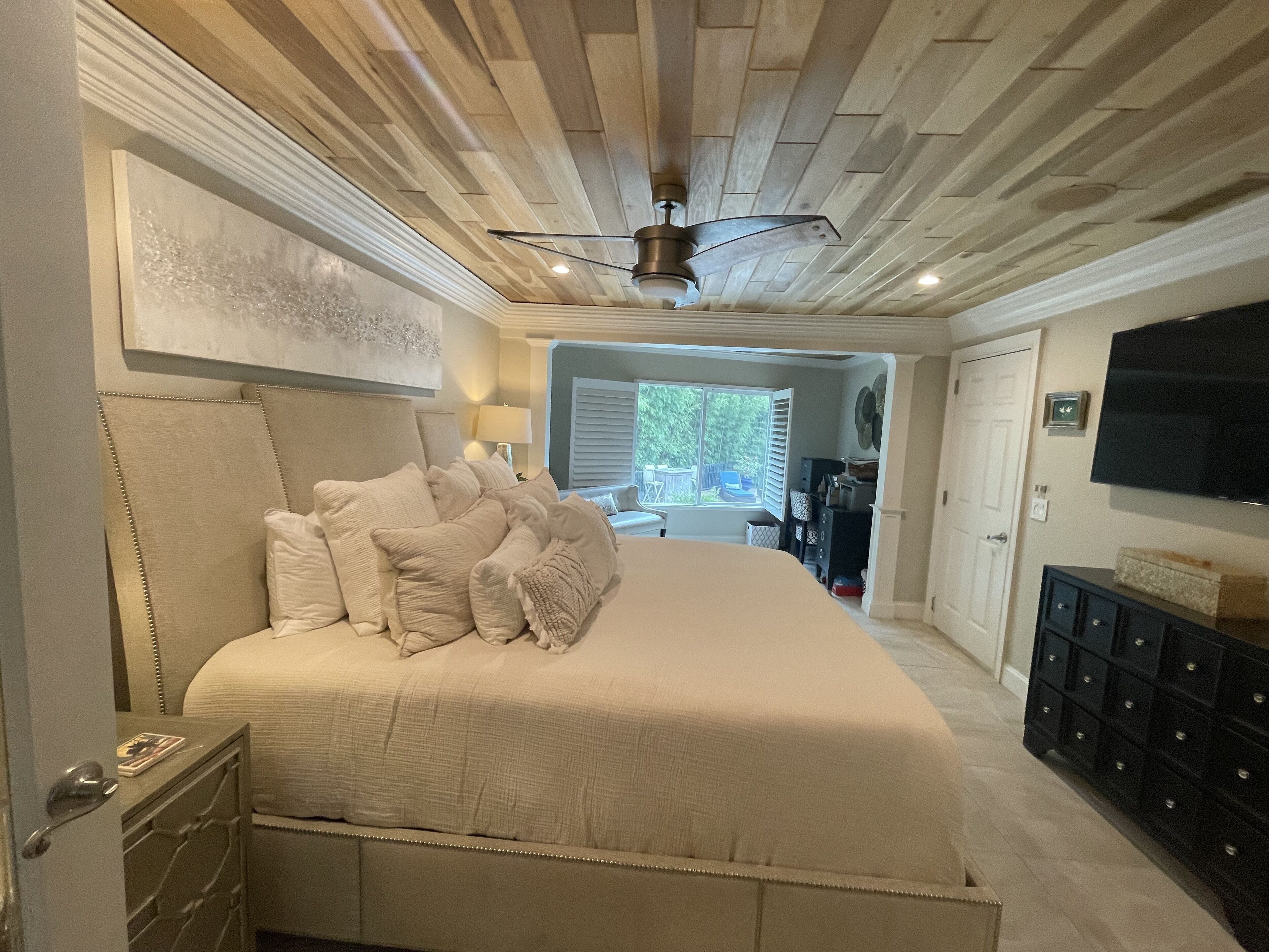 Une chambre avec un grand lit, un ventilateur de plafond, une télévision et une vue sur l’extérieur.