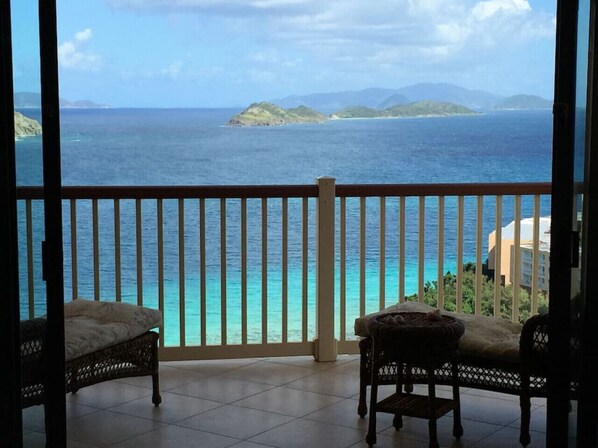 A balcony with two wicker chairs, a view of the ocean, and distant islands.