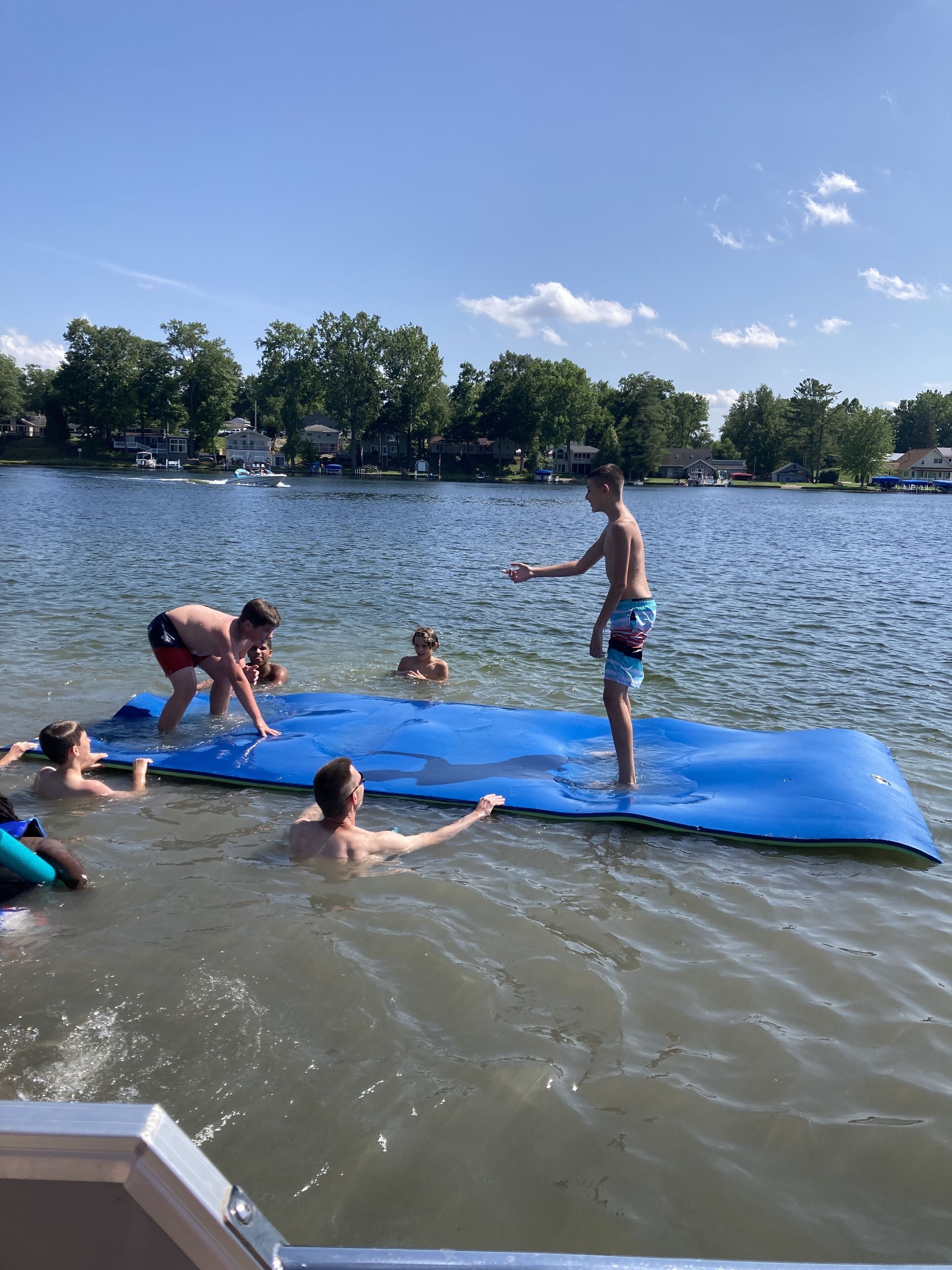 A group of people on a blue paddleboard in a lake with houses in the background.