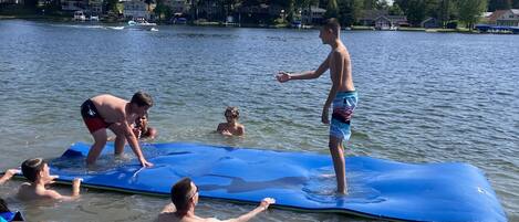 A group of people on a blue paddleboard in a lake with houses in the background.