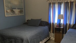 A bedroom with two beds, a nightstand with a lamp, a painting on the wall, and a window with curtains. - 3 bedrooms sleeps up to 10 people (Warsaw)