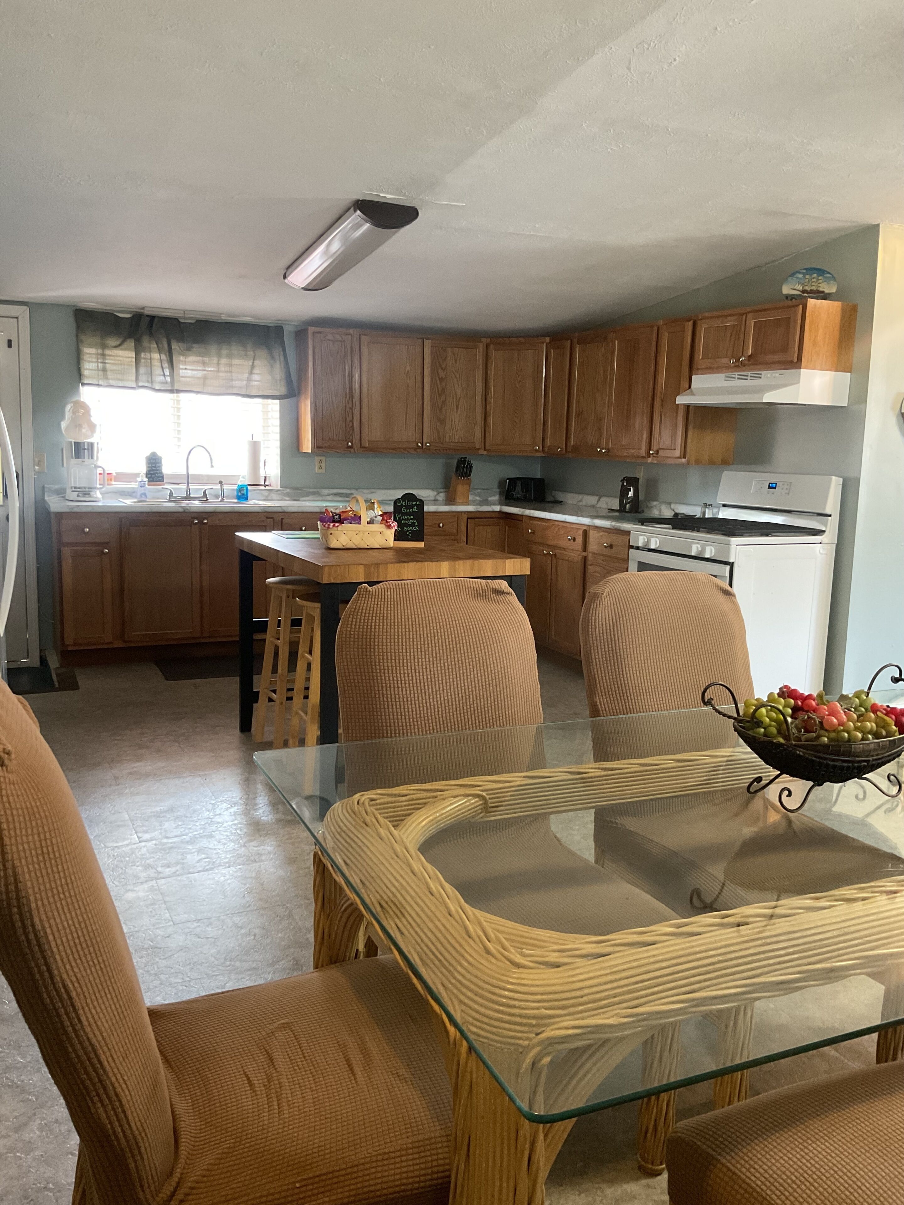 A kitchen with wooden cabinets, a central island, and a dining area with a glass table and wicker chairs.