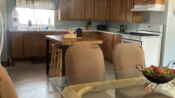 A kitchen with wooden cabinets, a central island, and a dining area with a glass table and wicker chairs.