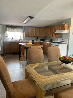 Een keuken met houten kastjes, een centraal eiland en een eethoek met een glazen tafel en rieten stoelen.
