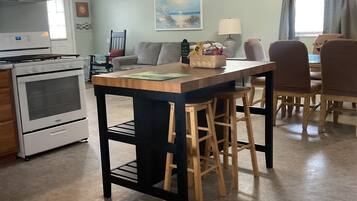 A kitchen with a central island, bar stools, a dining table with chairs, a ceiling fan, and a painting on the wall.