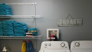 A laundry room with two white front-loading washers and dryers, a metal shelving unit with folded towels, and a laundry basket on the floor. - 3 bedrooms sleeps up to 10 people (Warsaw)