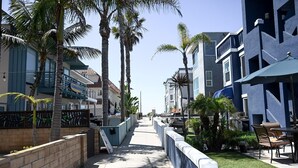 A coastal walkway lined with palm trees and modern buildings, featuring outdoor seating and a clear view of the ocean. - Amazing Proximity to the Beach and Bay with Direct Ocean Views! (San Diego)