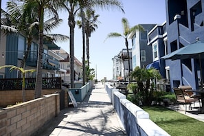 A coastal walkway lined with palm trees and modern buildings, featuring outdoor seating and a clear view of the ocean. - Amazing Proximity to the Beach and Bay with Direct Ocean Views! (San Diego)