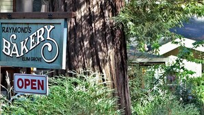 A sign for Raymond's Bakery with an 'OPEN' sign below it. - Raymond's Bakery - Creekside Cabin and Breakfast (Cazadero)