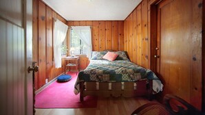 A wooden-paneled bedroom with a bed, a chair, and a small table. - Raymond's Bakery - Creekside Cabin and Breakfast (Cazadero)