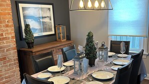 A dining area with a rectangular table set for six, surrounded by dark chairs. A wooden bench with a cushioned seat is against the wall, and a framed picture hangs above it. - Entire house 10 minute walk to The Falls and all Attractions! No Car Needed (Niagara Falls)