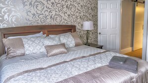 A neatly made bed with a patterned bedspread and pillows, a bedside lamp, and a door to another room. - Entire house 10 minute walk to The Falls and all Attractions! No Car Needed (Niagara Falls)