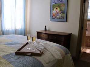 Una cama bien hecha con colcha, una mesita de noche de madera con lámpara y un cuadro en la pared.