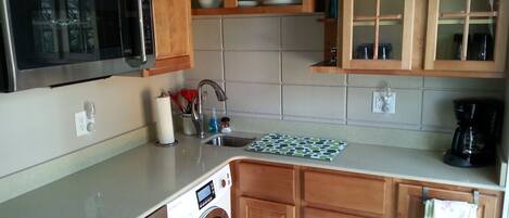 A kitchen with wooden cabinets, a stainless steel microwave, a washing machine, and a coffee maker.