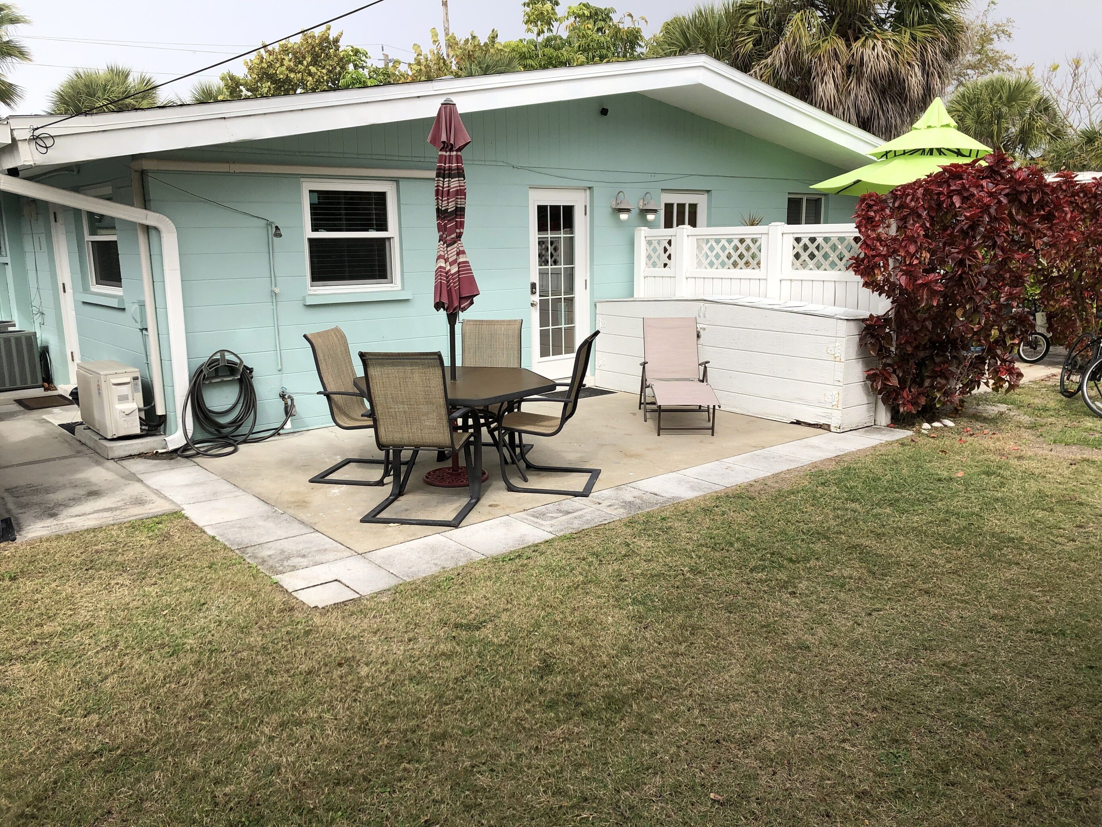 A house with a patio, a table with chairs, a covered umbrella, and a white fence.