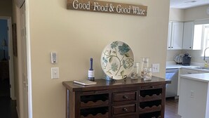 A kitchen with a wooden wine rack, a decorative plate, and a sign saying "Good Food & Good Wine". - Family & Pet-Friendly,  Near Beaches + Restaurants,  2BR, 2BA (Wilmington)