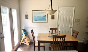 Un coin repas avec une table et des chaises en bois, un tableau accroché au mur et une porte donnant sur l’extérieur.