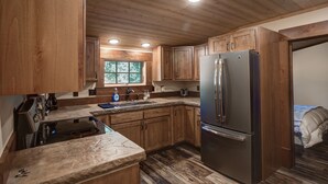 Une cuisine avec des meubles en bois, un réfrigérateur en acier inoxydable, un plan de travail en granit et une fenêtre donnant sur les arbres.