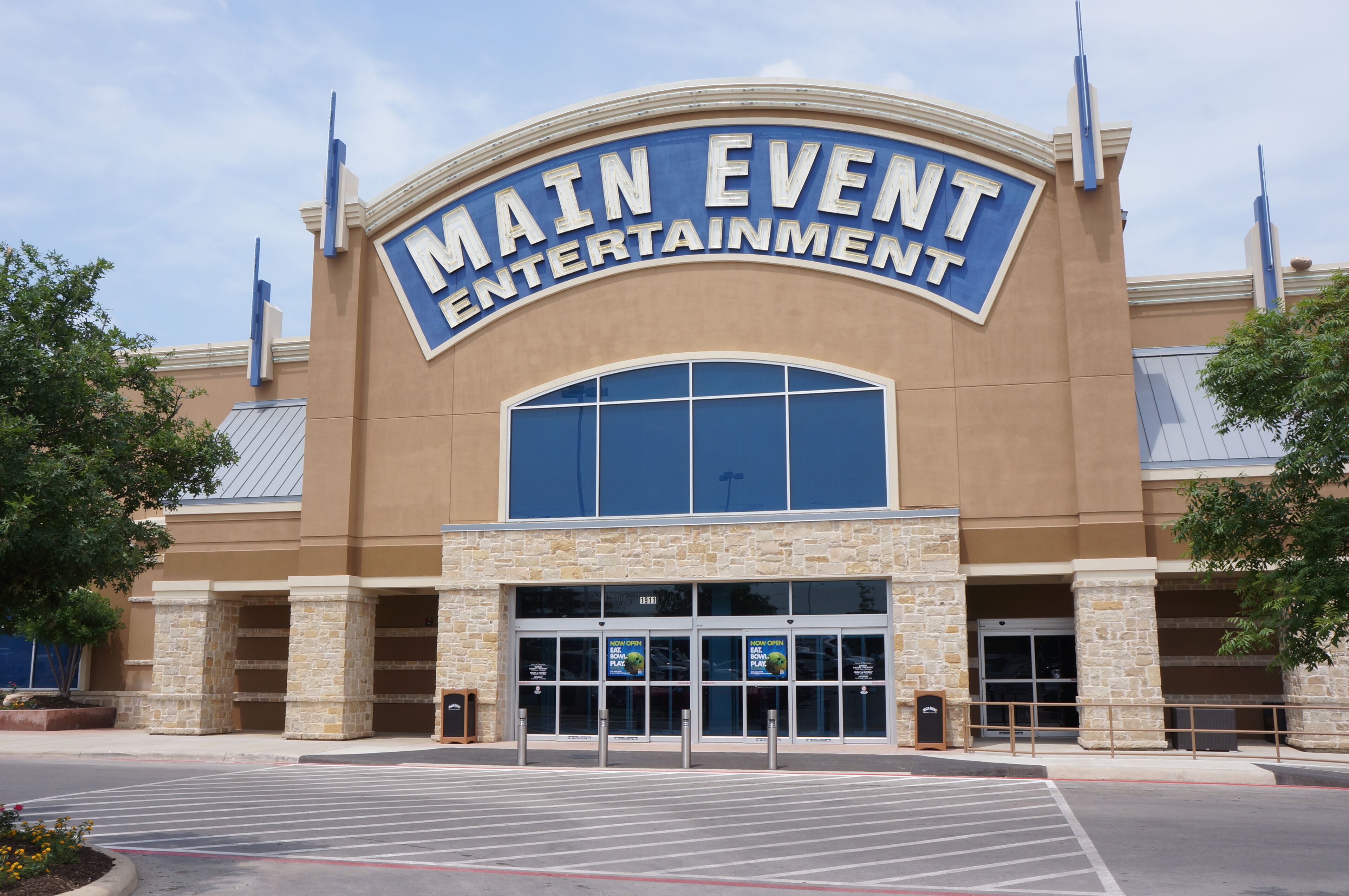 A Main Event Entertainment building with a large sign, stone pillars, and a parking lot.