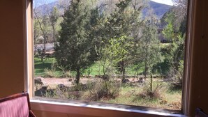 A room with a large window overlooking a forested area with mountains in the background. - Great Location in Cheyenne Cañyon, 3Bd, 1.5Bath, Private fenced yard and deck! (Colorado Springs)