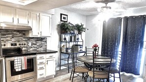 A kitchen with a stove, oven, and cabinets. There is a dining table with chairs and a ceiling fan. - Beachfront View from 9th Floor (South Padre Island)