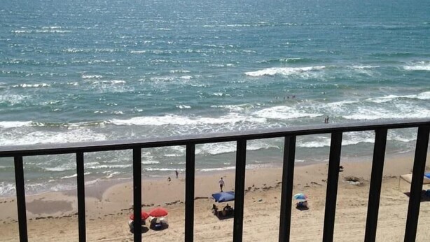 A beach with a view of the ocean, a sandy shore, and a few umbrellas. - Beachfront View from 9th Floor (South Padre Island)
