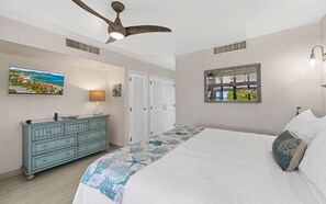 A bedroom with a bed, a dresser, a ceiling fan, a TV, and a window with a view.