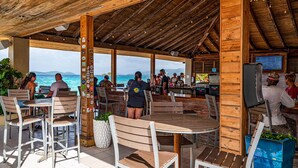 Un área de comedor al aire libre con mesas y sillas de madera, una barra y vista al océano.