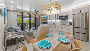 A modern kitchen with stainless steel appliances, a dining area with a wooden table set for four, and a large window overlooking a garden. - Sapphire Beach, Beach Level Condo, B Bldg, Bella Mar, Remodeled 2025, Generator (St. Thomas)