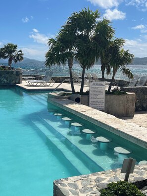A clear blue pool with lounge chairs and palm trees, with a sign indicating pool regulations.