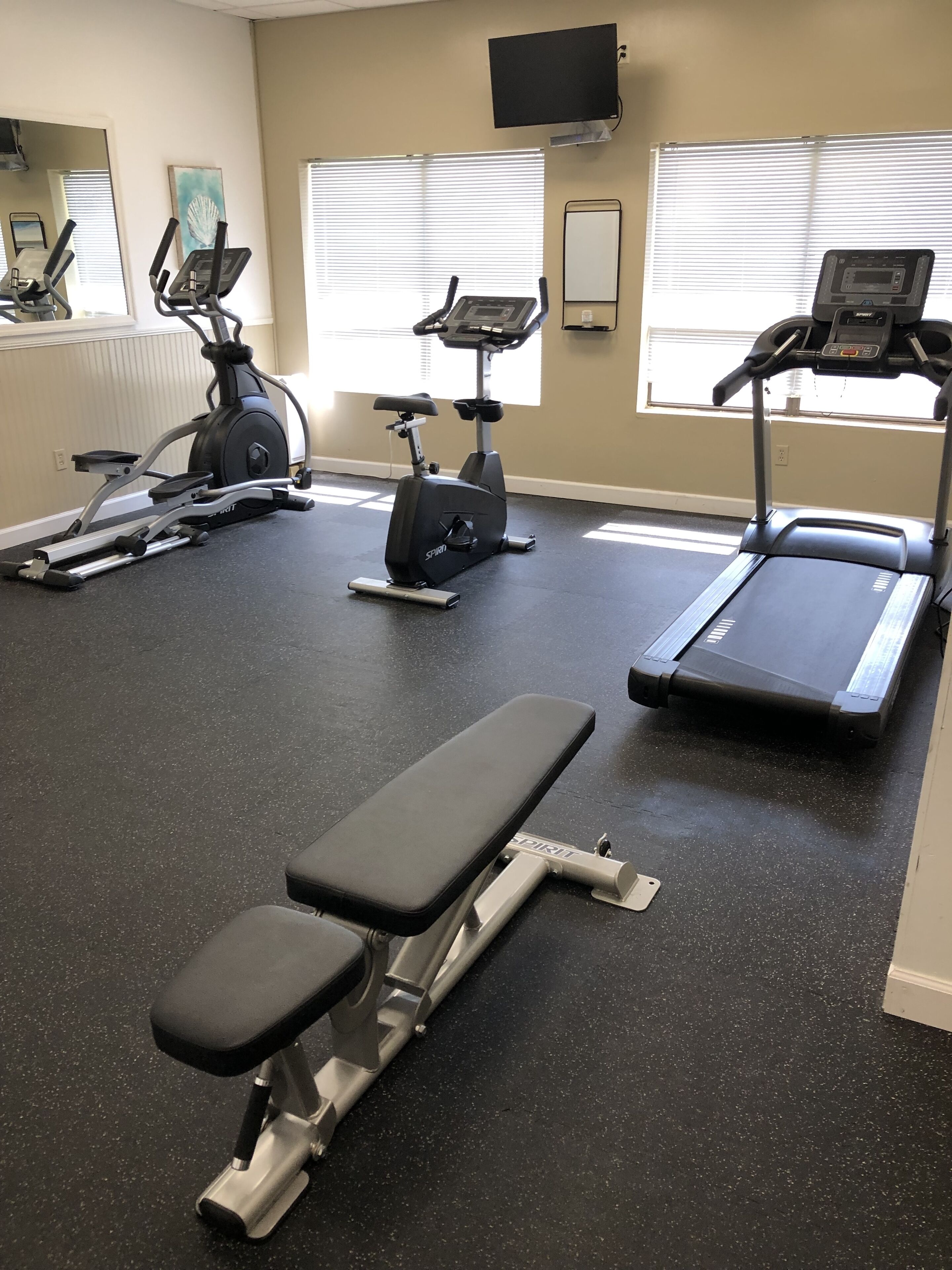 Une salle de sport équipée de tapis de course, d’un vélo elliptique et d’un banc de musculation.