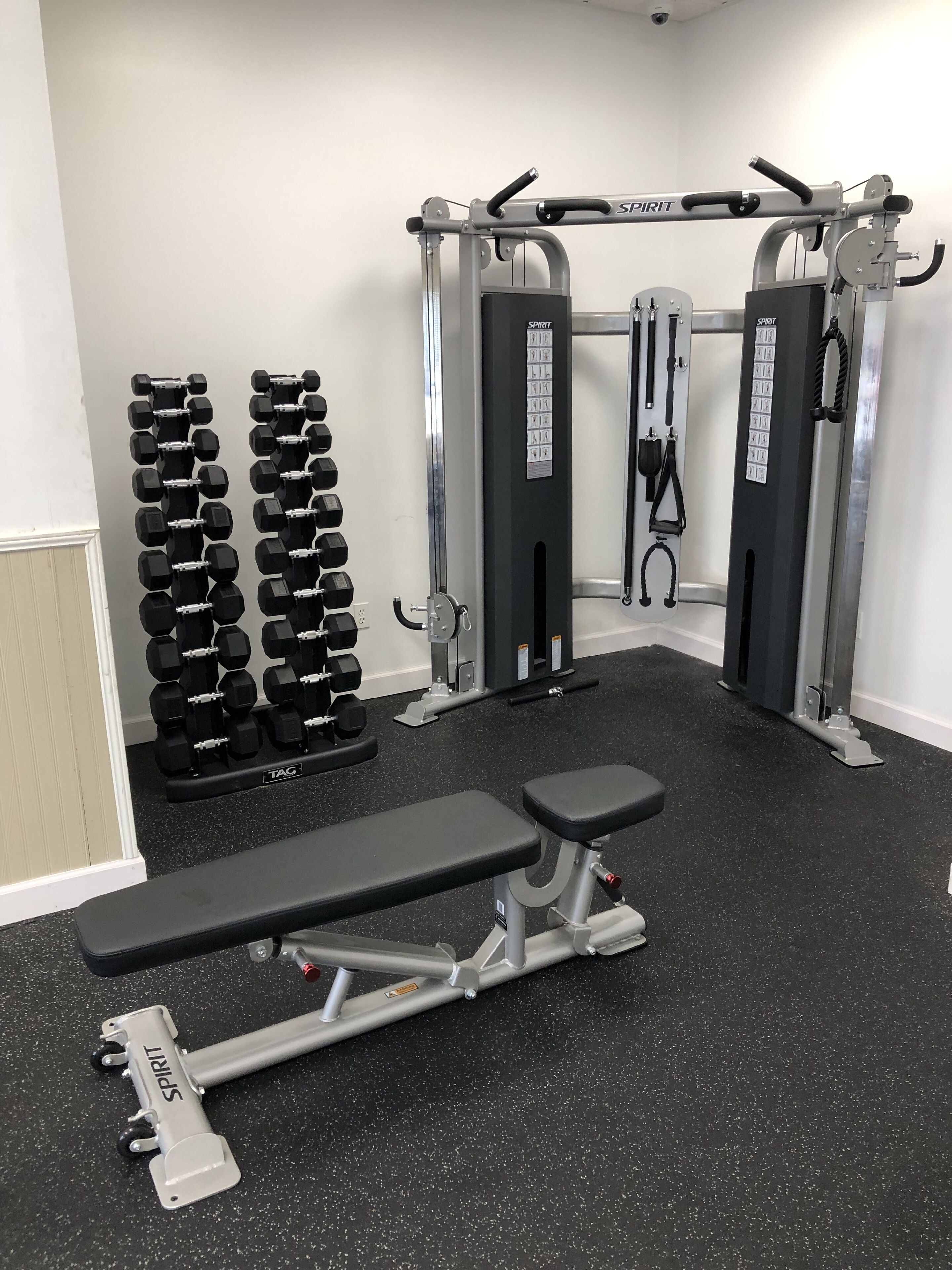 Une salle de sport équipée d’un banc de développé couché, d’haltères et d’une machine à câbles.