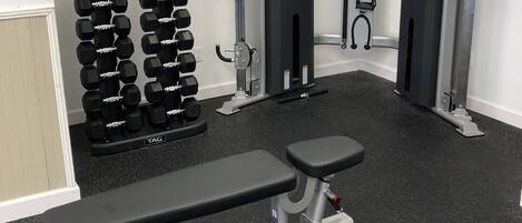 Une salle de sport équipée d’un banc de développé couché, d’haltères et d’une machine à câbles.
