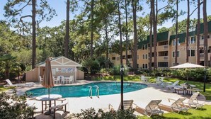 A hotel with a swimming pool surrounded by lounge chairs and a small building with a sign. - WALK TO THE BEACH!!  First floor condo, fully renovated (Hilton Head Island)
