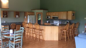 Une cuisine spacieuse dotée de meubles en bois, d’un îlot central avec des tabourets et d’un coin repas avec des chaises.