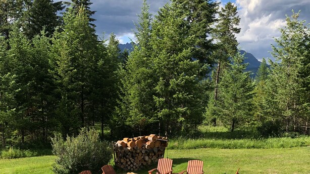 Un espace extérieur verdoyant, avec des fauteuils Adirondack en bois et un foyer en pierre.