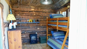 A rustic cabin interior with a bunk bed, wooden dresser, and a shelf with decorative items. - Casa Madre 3 bedroom/2 baths (Taos)