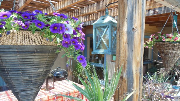 A rustic outdoor setting with hanging flower baskets, a lantern, and various potted plants. - Casa Madre 3 bedroom/2 baths (Taos)
