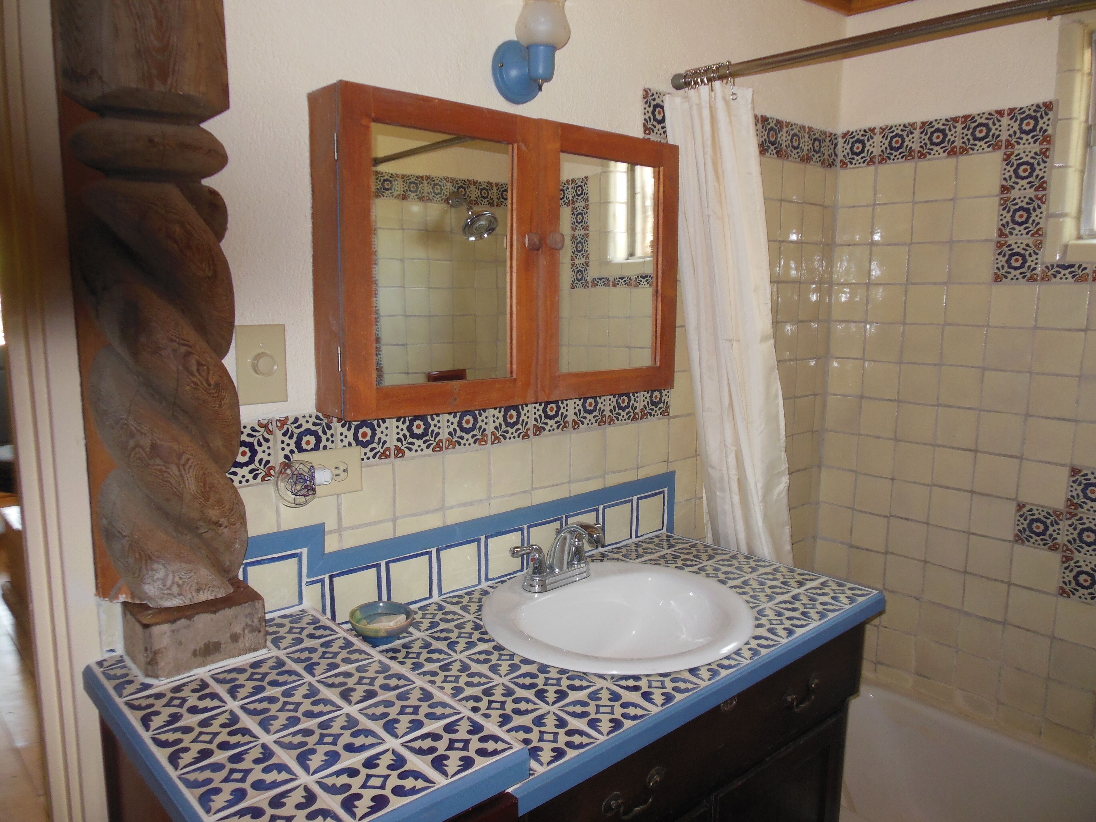 A bathroom with a white sink, blue and white patterned tiles, a wooden cabinet, and a mirror above the sink.