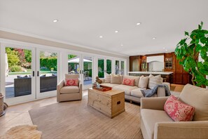 A spacious living room with a beige sofa, a wooden coffee table, and a large window overlooking a garden.