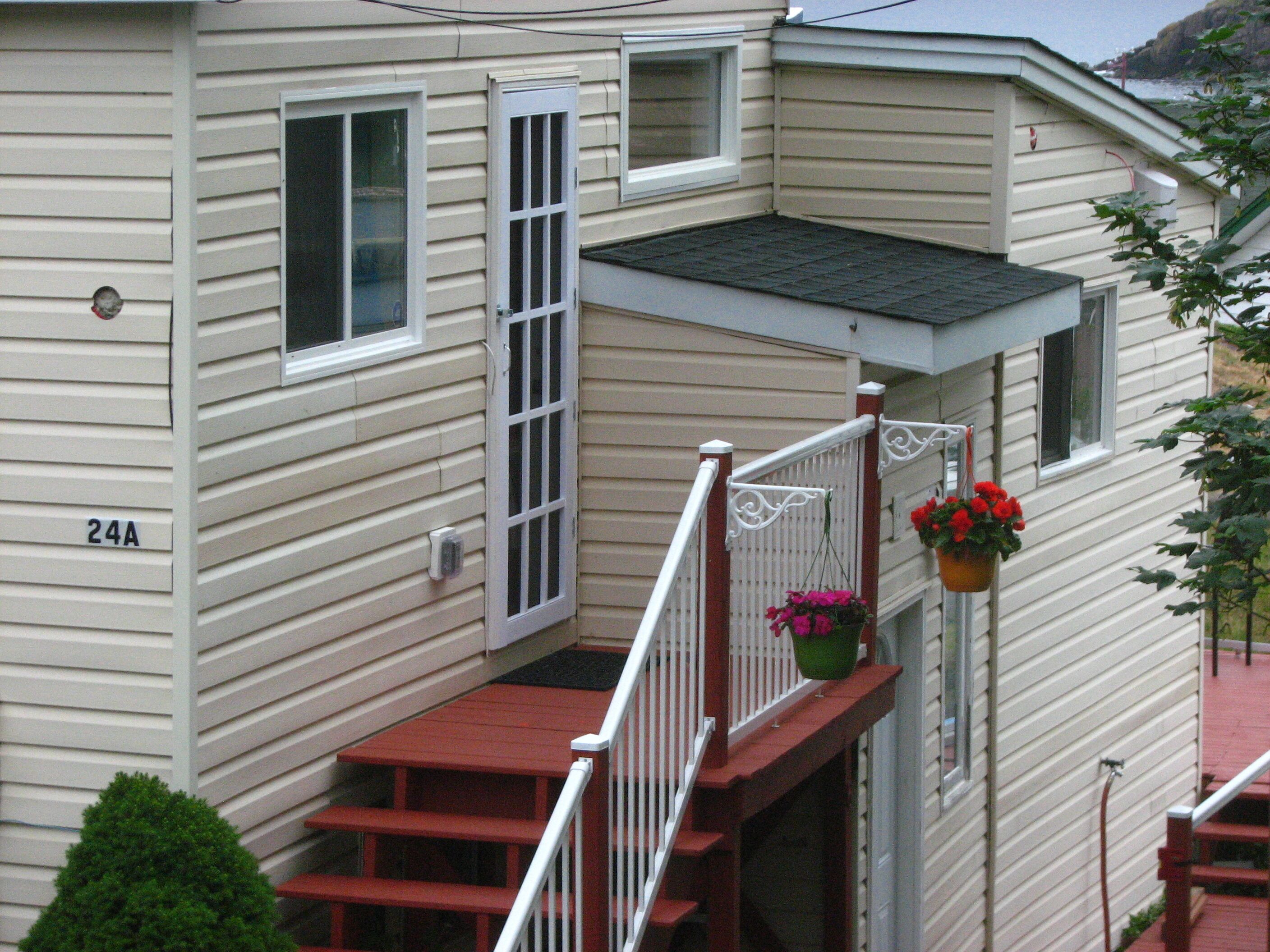 Une maison à deux étages avec un porche rouge à l’avant, un petit balcon doté d’une balustrade blanche et une fenêtre avec un volet blanc.