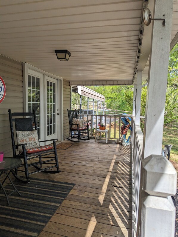 A covered porch with a rocking chair, a table, and a grill.