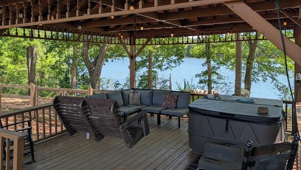 Une terrasse couverte avec un espace salon, un jacuzzi et une vue sur un lac.